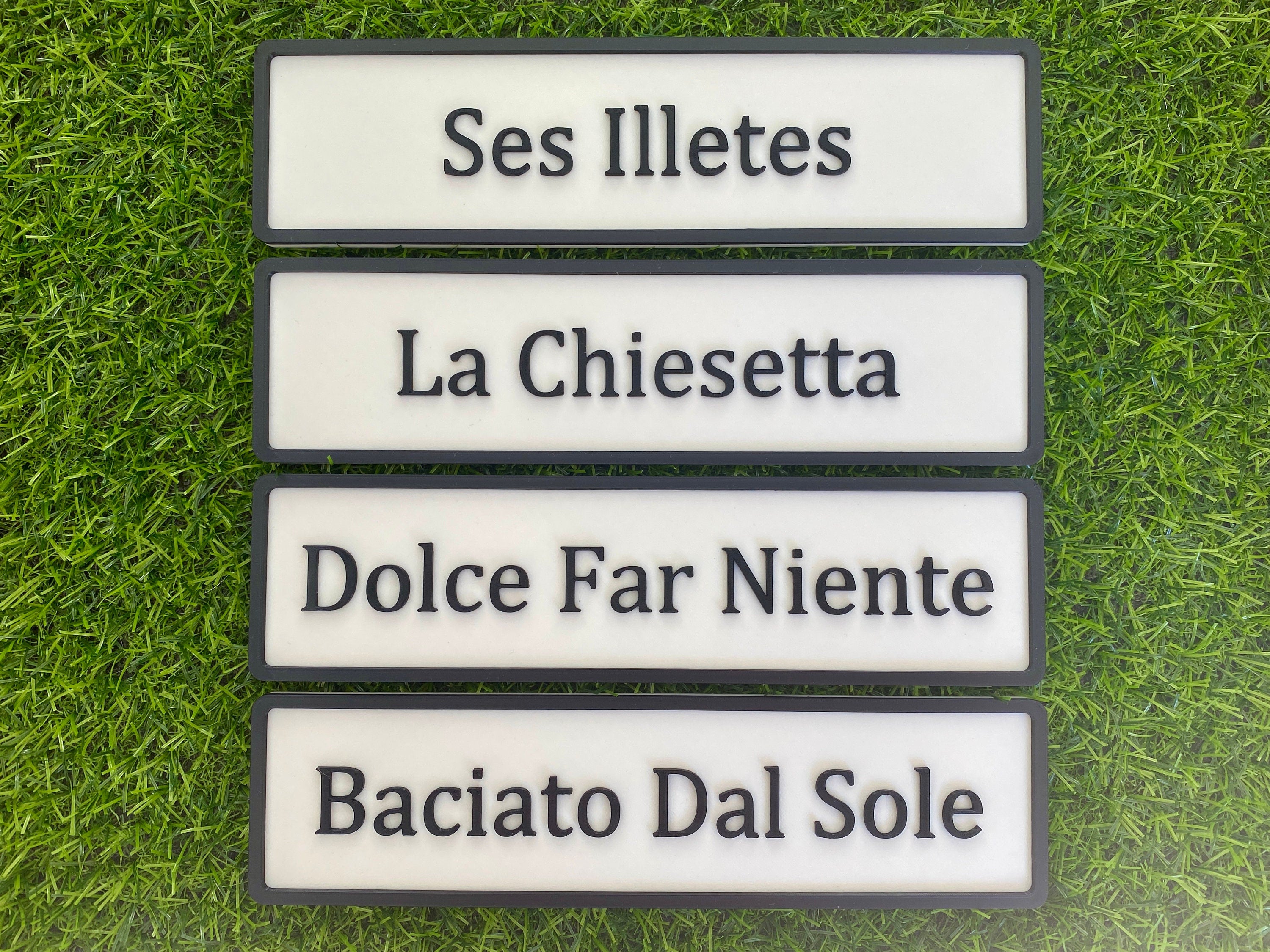 Four contemporary door signs stacked: Ses Illetes, La Chiesetta, Dolce Far Niente and Baciato Dal Sole