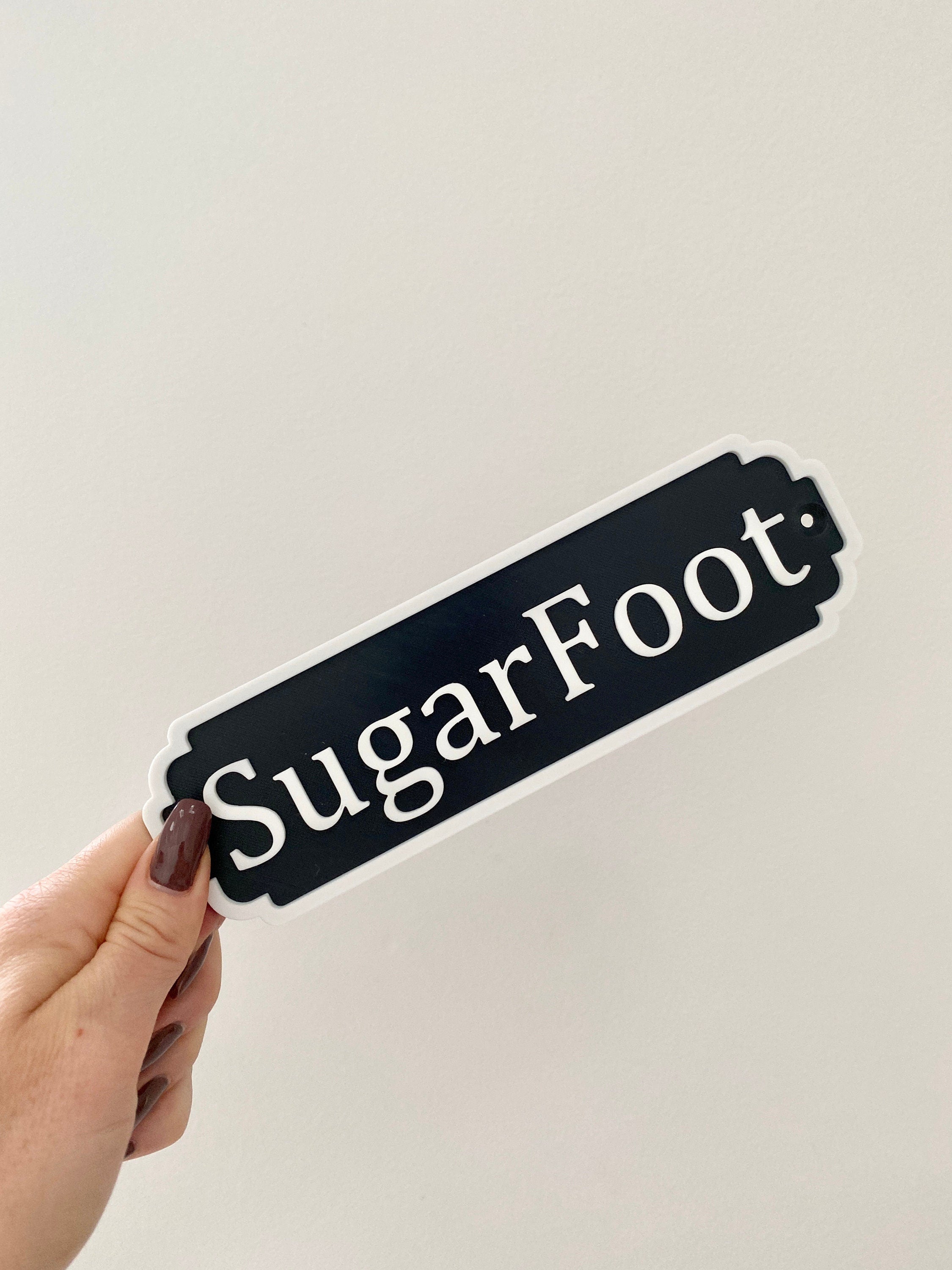 Black and white classic door sign reading SugarFoot held in hand