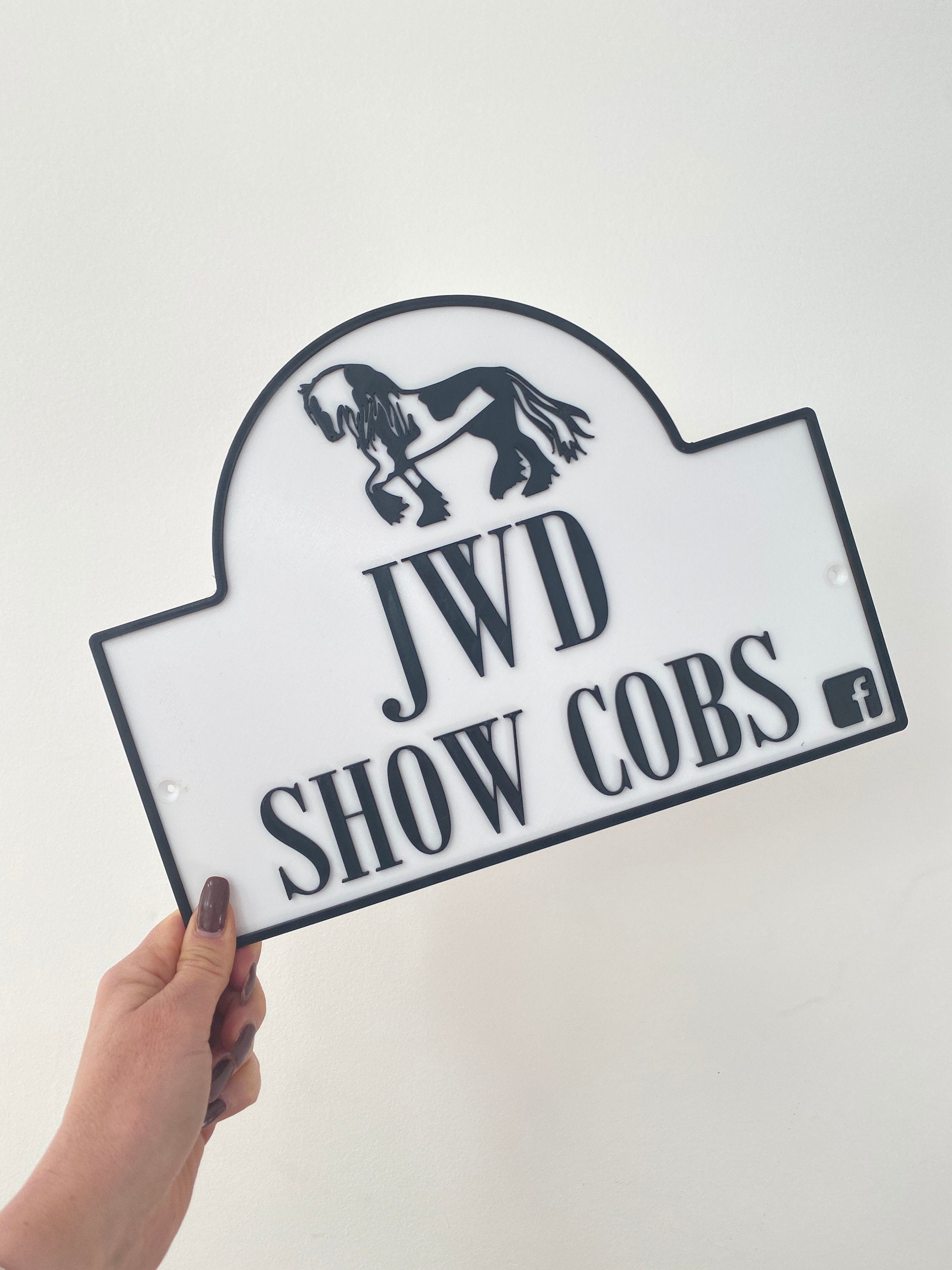 White dual colour sign reading JWD Show Cobs with black show cob motif