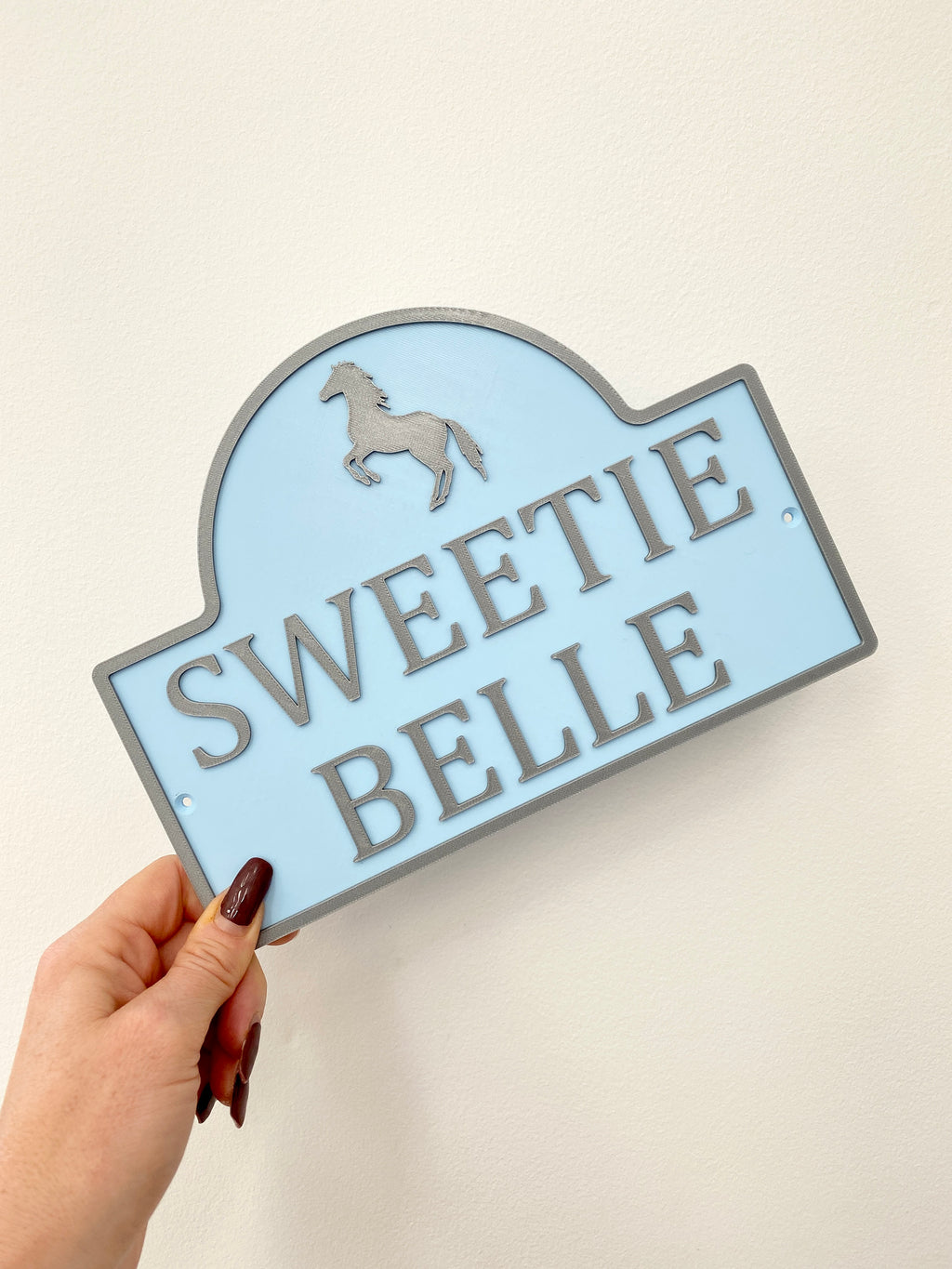 Pale blue dual colour sign reading Sweetie Belle with grey unicorn motif