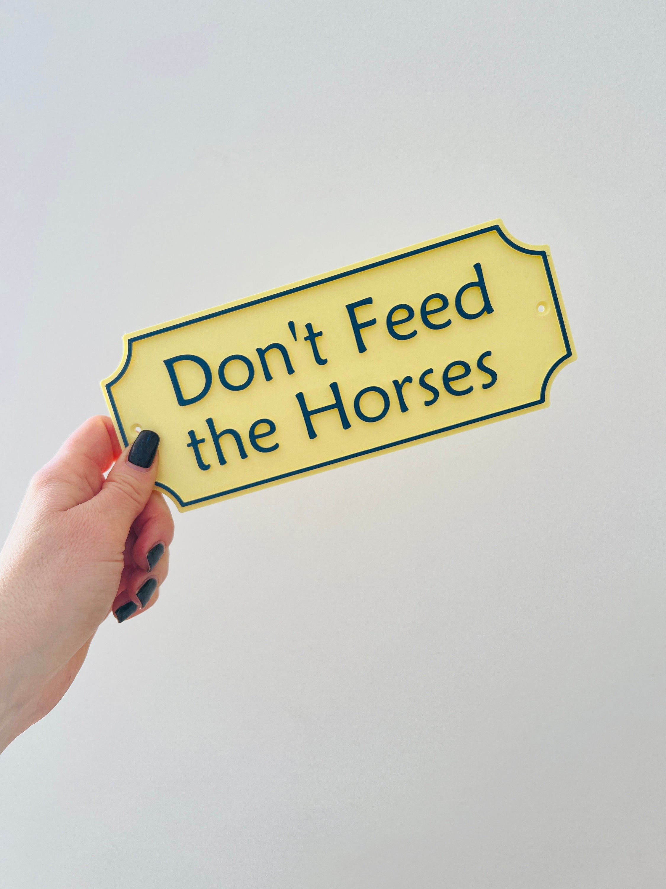 Pale yellow Don't Feed the Horses Emley sign held in hand